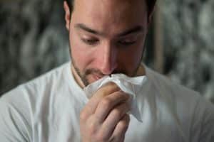 Man putting a tissue up to his red nose